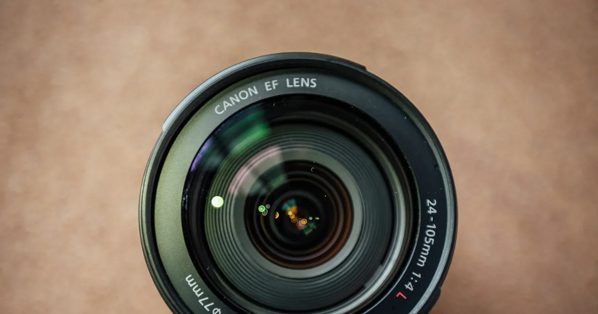 A photographer sitting at a desk reviewing images on a laptop screen next to a camera and a lens