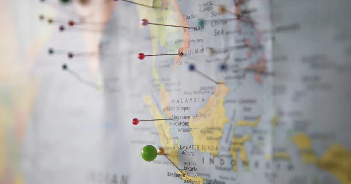 A world map with multiple coloured pins pushed into it